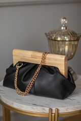 Stylish evening women's clutch bag black color with wooden closure on table in shop. Fashionable women's bag.