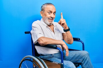 Sticker - Handsome senior man with beard sitting on wheelchair pointing finger up with successful idea. exited and happy. number one.