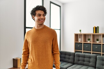 Wall Mural - Young hispanic man wearing casual clothes standing at home looking away to side with smile on face, natural expression. laughing confident.