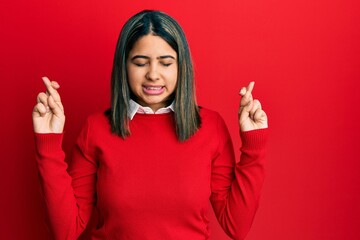 Wall Mural - Young latin woman wearing casual clothes gesturing finger crossed smiling with hope and eyes closed. luck and superstitious concept.