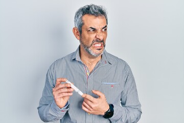 Poster - Handsome middle age man with grey hair holding glucometer device angry and mad screaming frustrated and furious, shouting with anger. rage and aggressive concept.