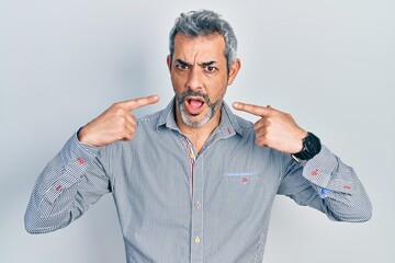 Wall Mural - Handsome middle age man with grey hair pointing mouth with fingers in shock face, looking skeptical and sarcastic, surprised with open mouth