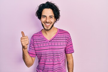 Wall Mural - Handsome hispanic man wearing casual pink t shirt smiling with happy face looking and pointing to the side with thumb up.