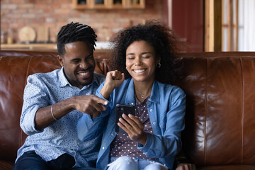 happy young african ethnicity multiracial couple looking at phone screen, reading email with amazing