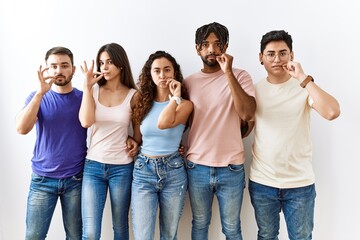 Sticker - Group of young people standing together over isolated background mouth and lips shut as zip with fingers. secret and silent, taboo talking