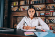 © teksomolika - Young woman in glasses writes in a notebook while sitting at the table