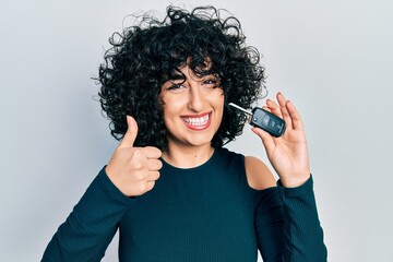 Sticker - Young middle east woman holding key of new car smiling happy and positive, thumb up doing excellent and approval sign