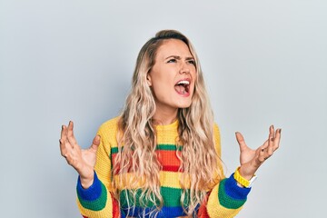 Sticker - Beautiful young blonde woman wearing colored sweater crazy and mad shouting and yelling with aggressive expression and arms raised. frustration concept.