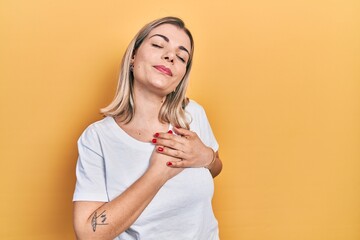 Beautiful caucasian woman wearing casual white t shirt smiling with hands on chest with closed eyes and grateful gesture on face. health concept.