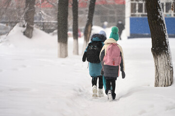 Winter city landscape. two schoolgirls go to school on a snow-covered trail. Snow is falling. Selective focus.