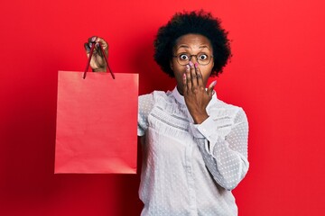 Wall Mural - Young african american woman holding shopping bags covering mouth with hand, shocked and afraid for mistake. surprised expression