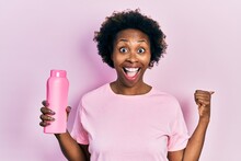 Young African American Woman Holding Shampoo Bottle Pointing Thumb Up To The Side Smiling Happy With Open Mouth