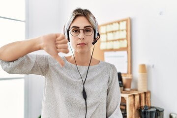 Sticker - Young beautiful woman working at the office wearing operator headset with angry face, negative sign showing dislike with thumbs down, rejection concept