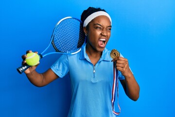 Sticker - African american woman with braided hair playing tennis holding racket and ball and winner medal angry and mad screaming frustrated and furious, shouting with anger. rage and aggressive concept.