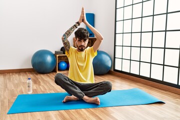 Sticker - Young hispanic man smiling confident training yoga at sport center.