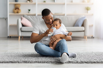 Childcare Concept. Loving African American Father Giving Bottle With Water To Baby