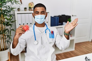 Wall Mural - Young indian doctor holding virus toy wearing safety mask celebrating achievement with happy smile and winner expression with raised hand