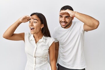 Poster - Young interracial couple standing together in love over isolated background very happy and smiling looking far away with hand over head. searching concept.