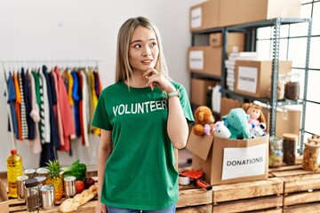 Sticker - Asian young woman wearing volunteer t shirt at donations stand with hand on chin thinking about question, pensive expression. smiling and thoughtful face. doubt concept.