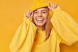 © wayhome.studio  - Happy playful young woman smiles broadly shows white teeth keeps hands on hat dressed in casual jumper expresses sincere emotions being in good mood isolated over yellow background. Joy concept