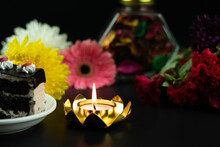 Tealight Candle Glowing In Golden Yellow Lotus Shaped Decorative Holder With Fresh Colorful Flowers On Dark Black Background. Theme For Merry Christmas, Happy New Year Or Shubh Deepawali