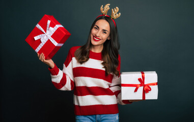 Wall Mural - Close up photo of a beautiful smiling trendy woman with Сhristmas reindeer antlers on her head while she holding gift boxes in hands and having fun