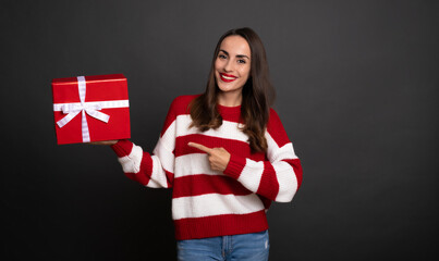 Wall Mural - Beautiful smiling modern young girl with gift box in hand is pointing on present