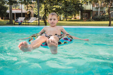 Boy Enjoying Summer Day On While Floating In Pool On Inflatable Ring
