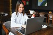 © Serhii - Photo portrait of gorgeous attractive woman working on laptop typing sitting in cafe drinking coffee