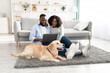 Black couple at home using laptop relaxing with dog