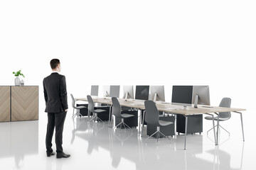 Poster - Businessman standing in modern white coworking office interior with computers, equipment, reception desk, wooden furniture and reflections on floor. Mock up place.