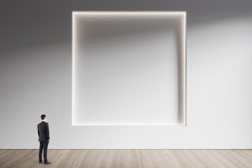 Poster - Businessman standing in minimalistic concrete and wooden interior with abstract clean square frame on wall. Mock up. Exhibition, gallery and art concept.