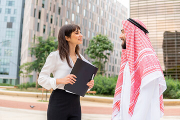 Satisfied arab businessman and young beautiful female assistant standing on city street and talking