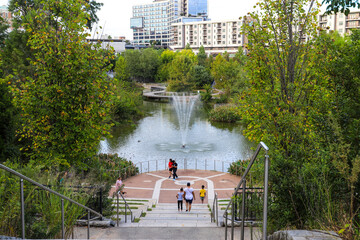 Wall Mural - a gorgeous shot of the green lake with water fountain in the center of the water, green and autumn colored trees with African American people standing near the lake at Historic Fourth Ward Park