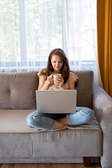 Wall Mural - A young woman is drinking a cup of coffee during working from home.