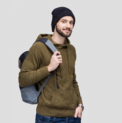 Young handsome man with backpack isolated on gray background. Smiling student or businessman winter portrait. Cool guy going on travel.