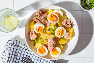 Canvas Print - Tuna and potato salad with egg and green onions in white bowl on white tile background. Healthy vegetarian food, fitness meal.