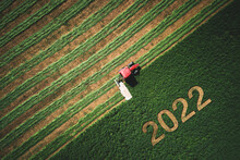 2022 Happy New Year Concept And Red Tractor Mowing Green Field