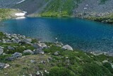 Fototapeta Natura - Aerial drone view of alone woman traveler in dress and hat watching on Seven colored mountain glacial lake, summer landscape: high peaks, snow, stones. Arkhyz, Caucasus, Karachay-Cherkessia, Russia