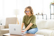 © Andrii - Woman glasses using laptop computer while sitting sofa with big window on background at home interior