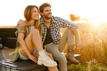 Young white couple hugging and smiling while sitting in trunk