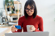 © Westend61 - Freelancer with credit card holding coffee mug looking at laptop