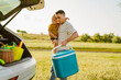Young father holding his son and cooler bag by car trunk outdoors