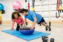 Smiling Female Fitness Instructor Assisting Disabled Man Exercising On Balance Ball In Gym