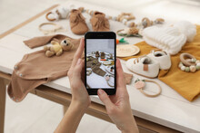 Woman Taking Picture Of Baby Clothes At White Wooden Table, Closeup