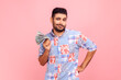 © khosrork - Portrait of arrogant wealthy bearded man in casual style blue shirt standing showing wad of money, looking at camera with proud expression, income. Indoor studio shot isolated on pink background.