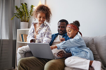 Wall Mural - Portrait of smiling African-American father using laptop with two daughters, copy space