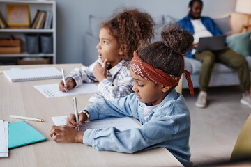 Wall Mural - Side view portrait of two African-American girls doing homework while sitting at desk in cozy home