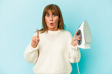 Middle age caucasian woman holding a iron isolated on blue background having some great idea, concept of creativity.