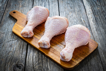 Raw chicken drumsticks on cutting board with seasonings on wooden table
